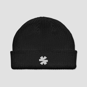 A black ribbed knit beanie hat with a folded cuff, featuring a small white embroidered asterisk logo on the front, set against a solid light gray background.