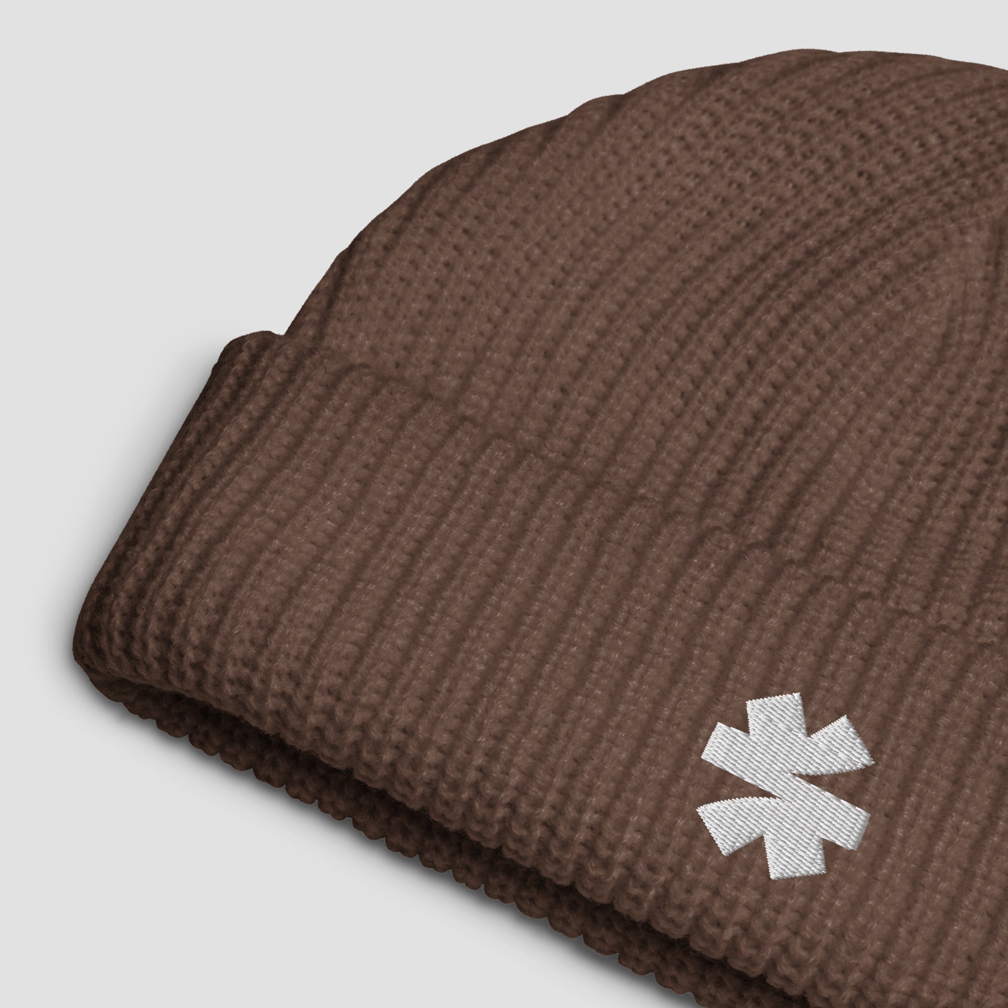 Close-up details of a ribbed knit beanie with small white embroidered asterisk logo set against a light gray background.