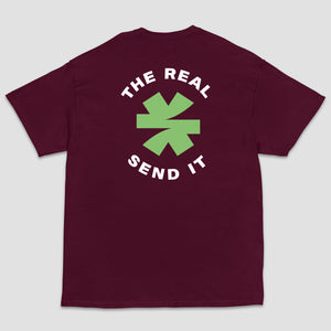 A maroon short-sleeve t-shirt shown from the back, featuring a green and black logo with the text 'THE REAL SEND IT' centered around a green asterisk set on a light gray background.