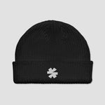 A black ribbed knit beanie hat with a folded cuff, featuring a small white embroidered asterisk logo on the front, set against a solid light gray background.