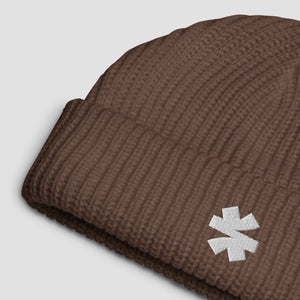 Close-up details of a ribbed knit beanie with small white embroidered asterisk logo set against a light gray background.
