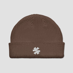 A brown ribbed knit beanie hat with a folded cuff, featuring a small white embroidered asterisk logo on the front, set against a light gray background.