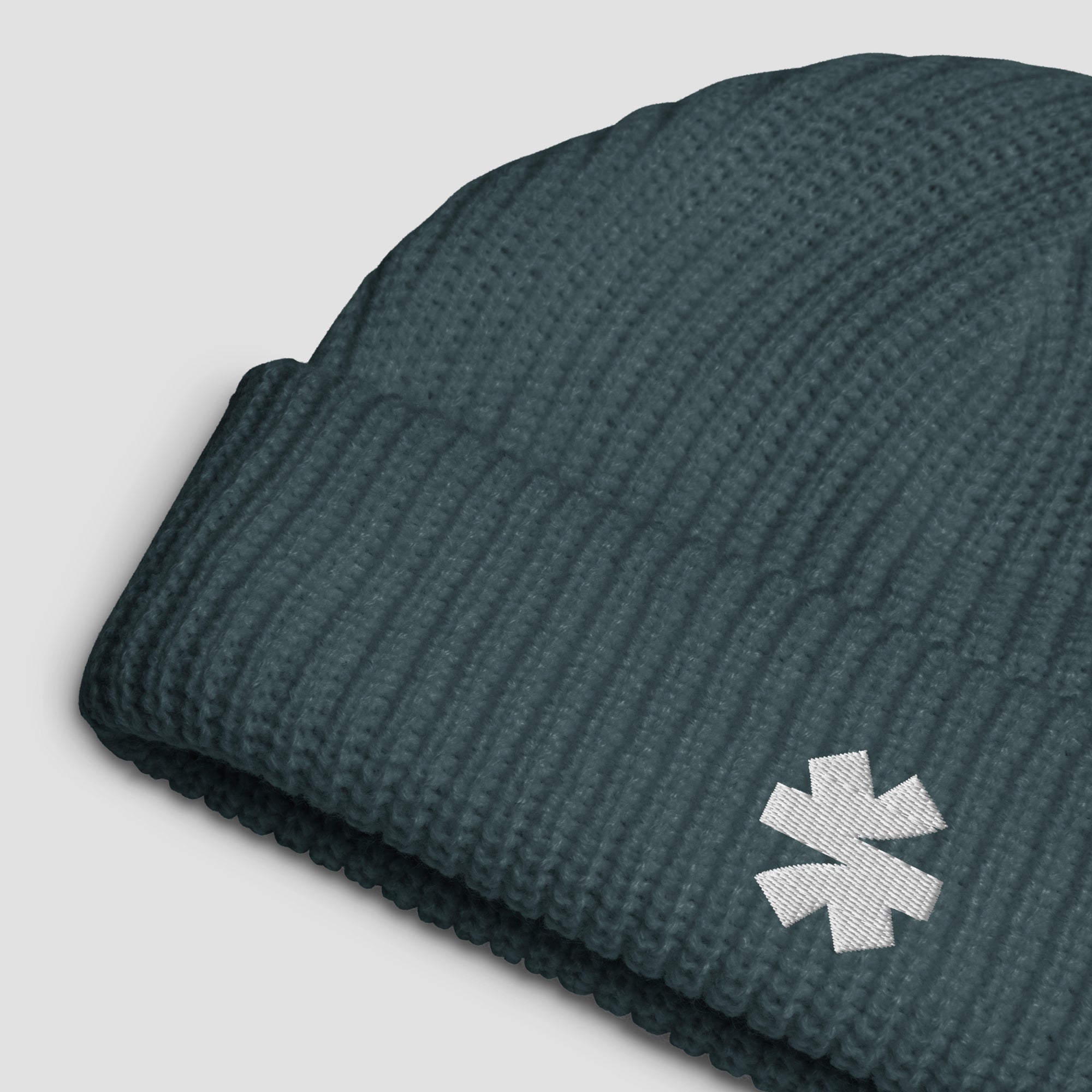 Close up details of a ribbed knit beanie with a white embroidered asterisk logo on a light gray background.