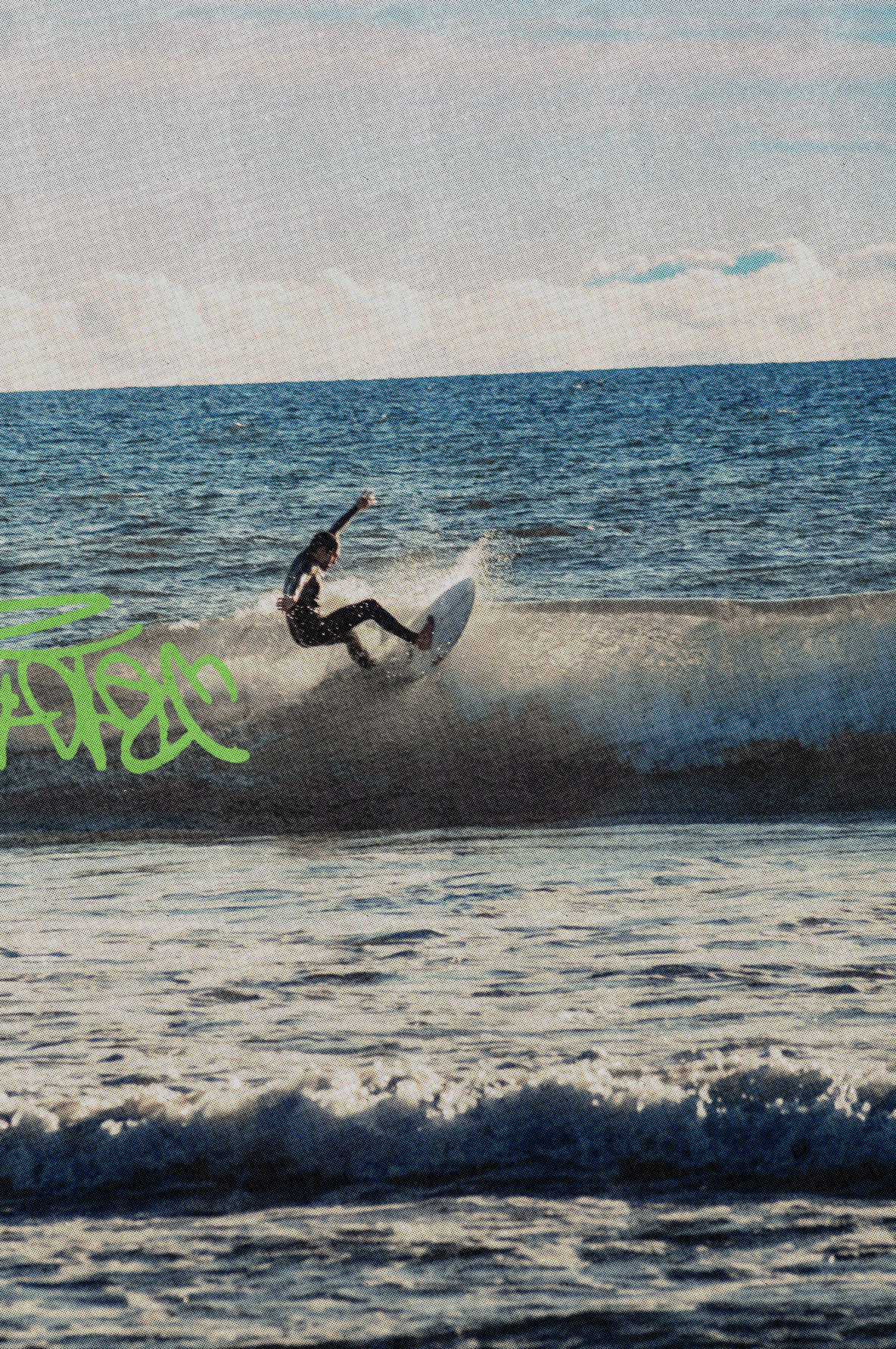 A surfer in a black wetsuit rides a wave on a white surfboard, with ocean water, a pale sky, and a bright green graffiti-style graphic overlay on the left side.